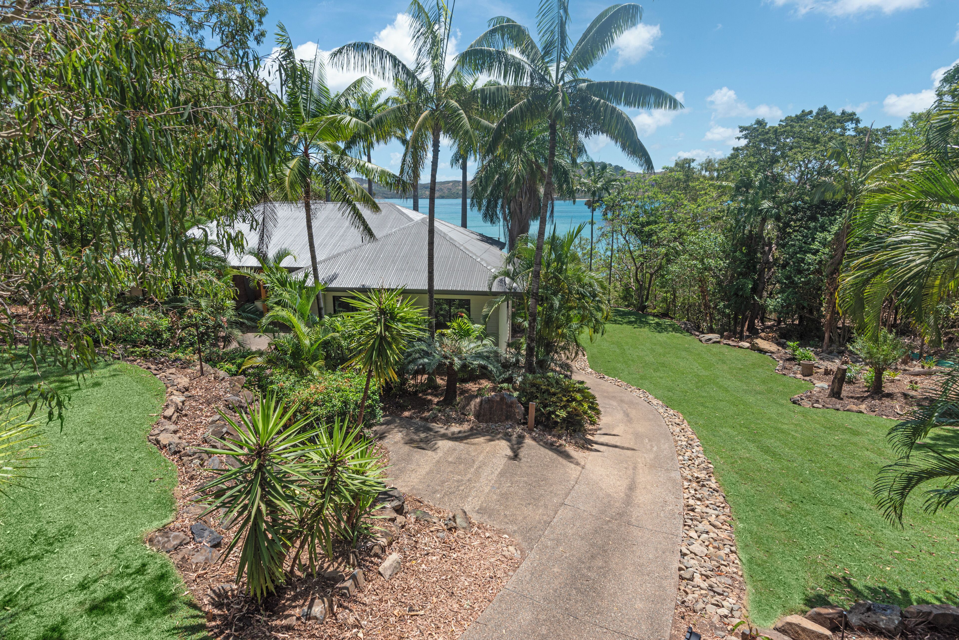 A tropical garden with a house, palm trees, and a clear blue sky.