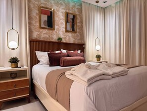 Une chambre élégante, dotée d’un grand lit, d’une tête de lit en bois, de deux tables de chevet avec des lampes et d’un miroir décoratif au mur.