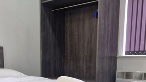 Un lit bien fait, avec une serviette blanche roulée, une armoire en bois foncé et une fenêtre ornée de rideaux violets.