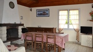 Ein Essbereich mit Tisch für vier Personen, Kamin, Fernseher und einem fenster mit Vorhängen.