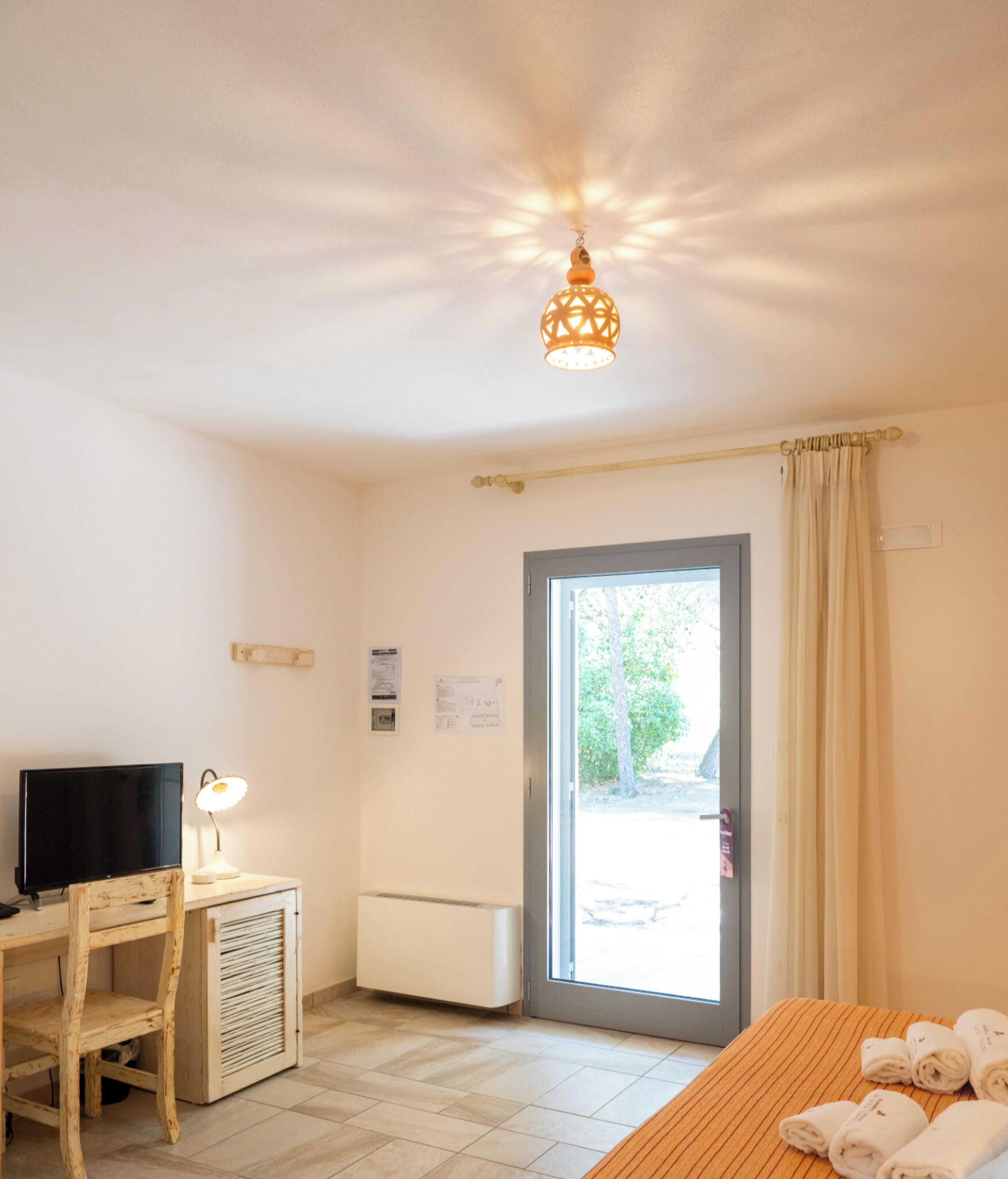 A room with a television, desk, chair, heater, and a bed with towels.