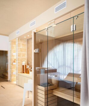 Une chambre moderne avec un lit entouré de parois de verre, un bureau en bois, un mur en pierre et une chaise blanche.