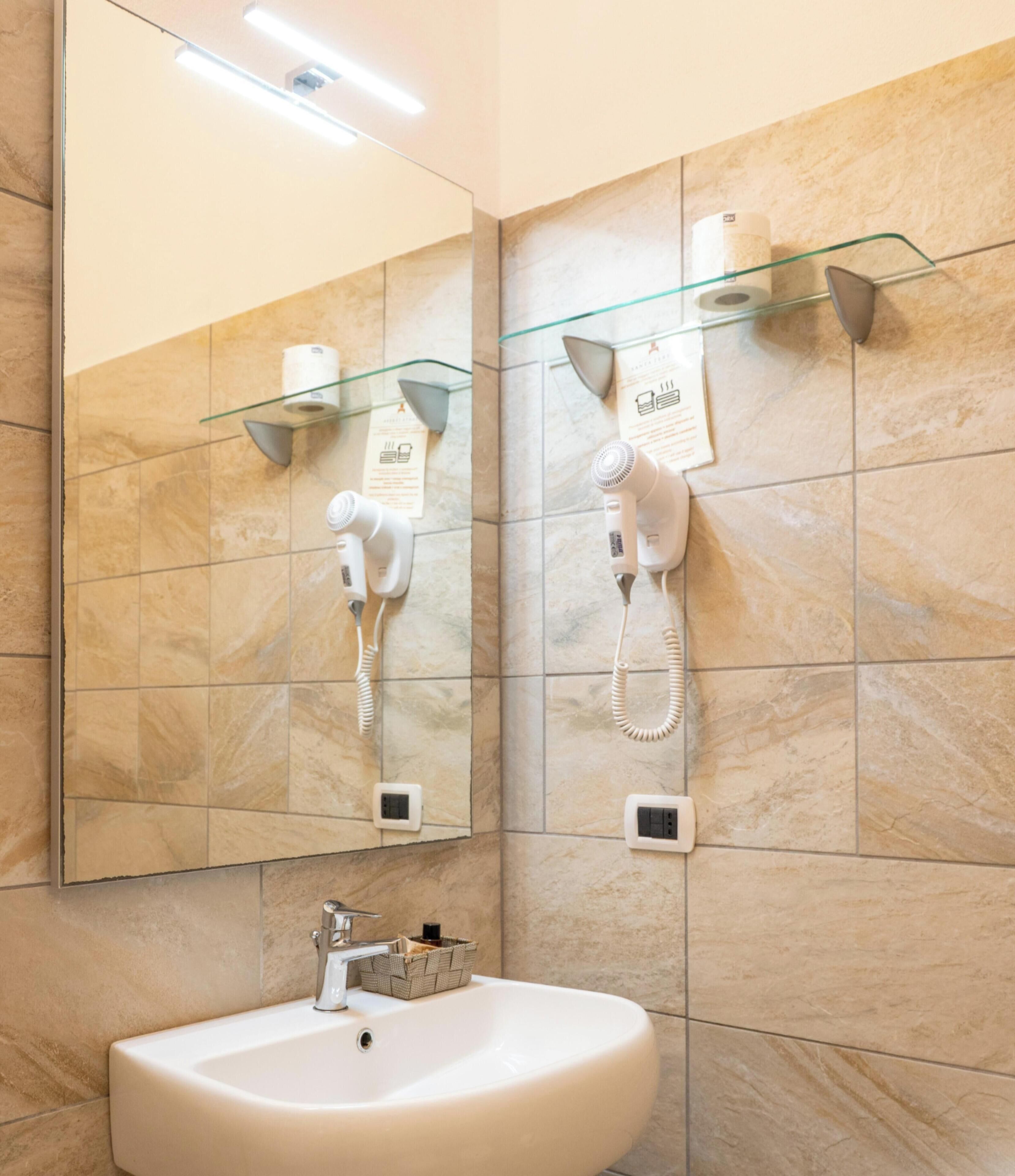Un baño con un lavabo, dos secadores de pelo sujetos a la pared y un espejo encima.