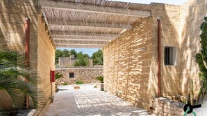 Een erf met stenen muren, een pergola en uitzicht op het omliggende landschap.