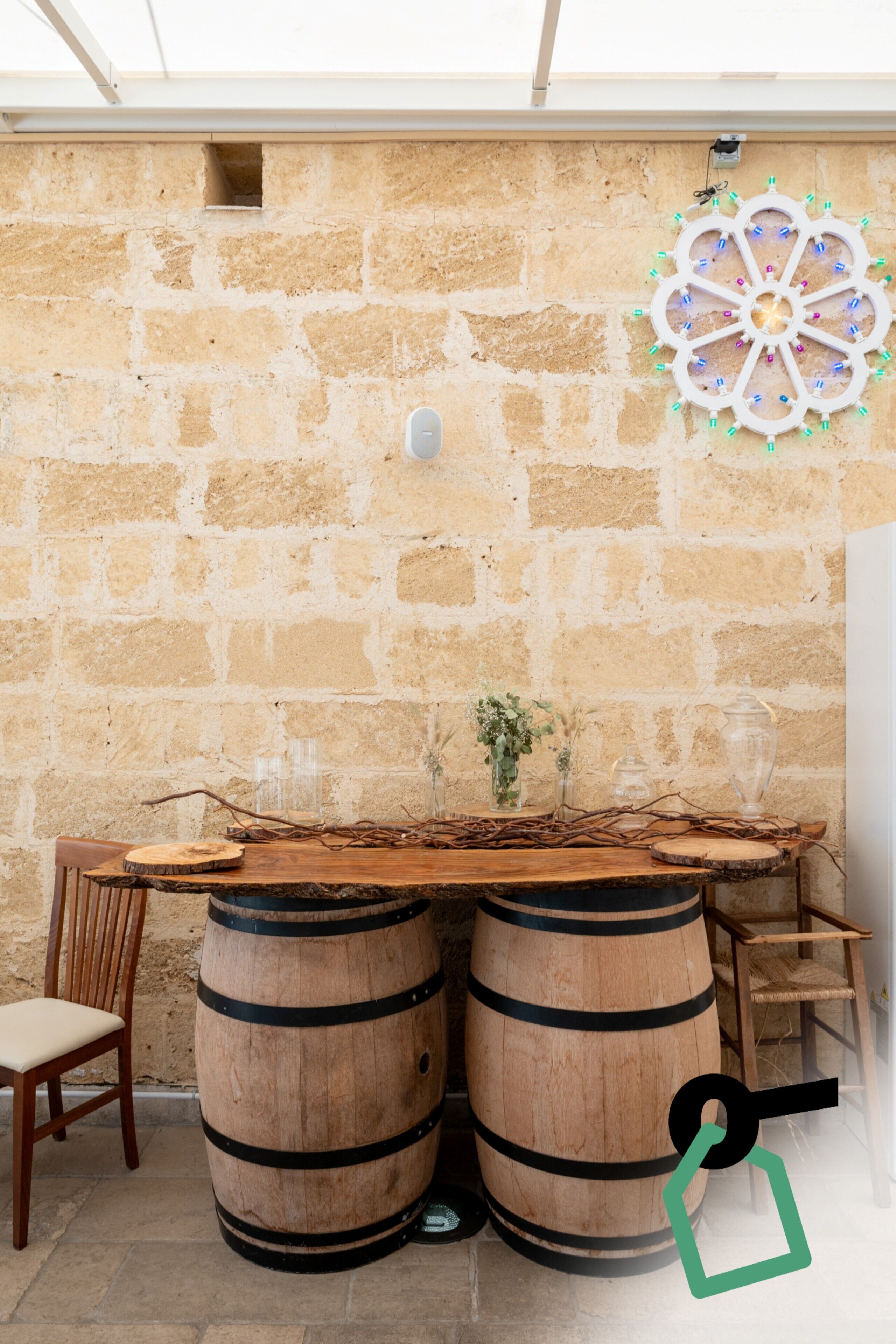 A rustic outdoor seating area with a stone wall backdrop, wooden barrels, and a decorative wall piece.