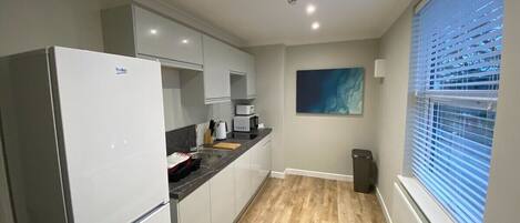 A modern kitchen with white cabinets, a built-in oven, and a window with blinds.