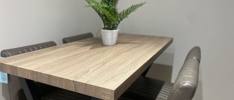 Een eettafel met een licht houten afwerking, gecombineerd met donker leren stoelen. Een kleine potplant staat op de tafel.