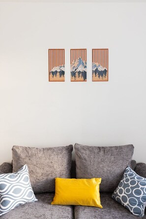 A grey sofa with three patterned cushions and three framed artworks on the wall. - Spacious 4-Bed Home Near Leeds Centre & Links (West Yorkshire)