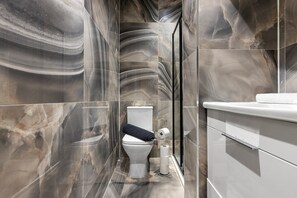 A bathroom with a marble wall, a toilet, a bidet, and a white sink. - Spacious 4-Bed Home Near Leeds Centre & Links (West Yorkshire)