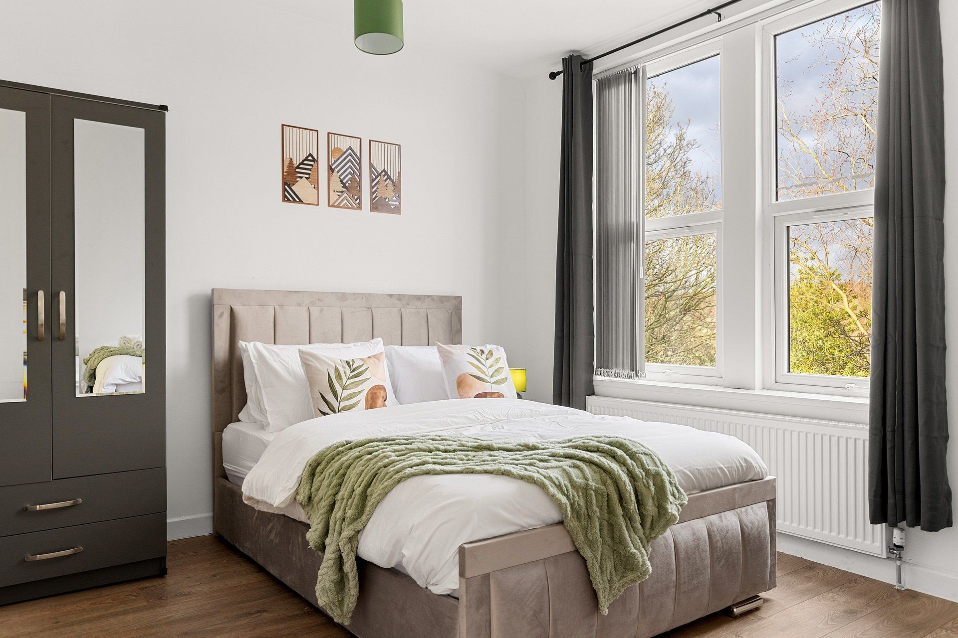 A bedroom with a bed, a wardrobe, a window with curtains, and wall art.