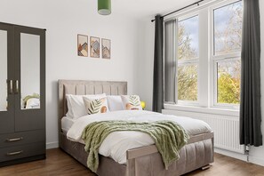 A bedroom with a bed, a wardrobe, a window with curtains, and wall art. - Spacious 4-Bed Home Near Leeds Centre & Links (West Yorkshire)