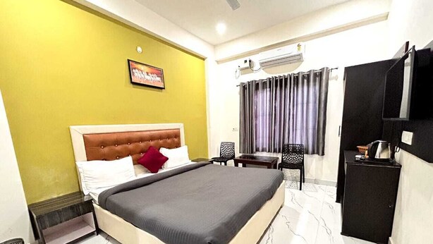 A hotel room with a bed, a small table, a chair, a TV, and an air conditioning unit. - Archana Home Stay-Best Hotel in varanasi (Varanasi)