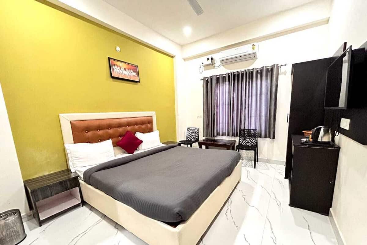 A hotel room with a bed, a small table, a chair, a TV, and an air conditioning unit.