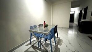 A dining area with a glass table and blue chairs, a red vase, and a potted plant. - Archana Home Stay-Best Hotel in varanasi (Varanasi)