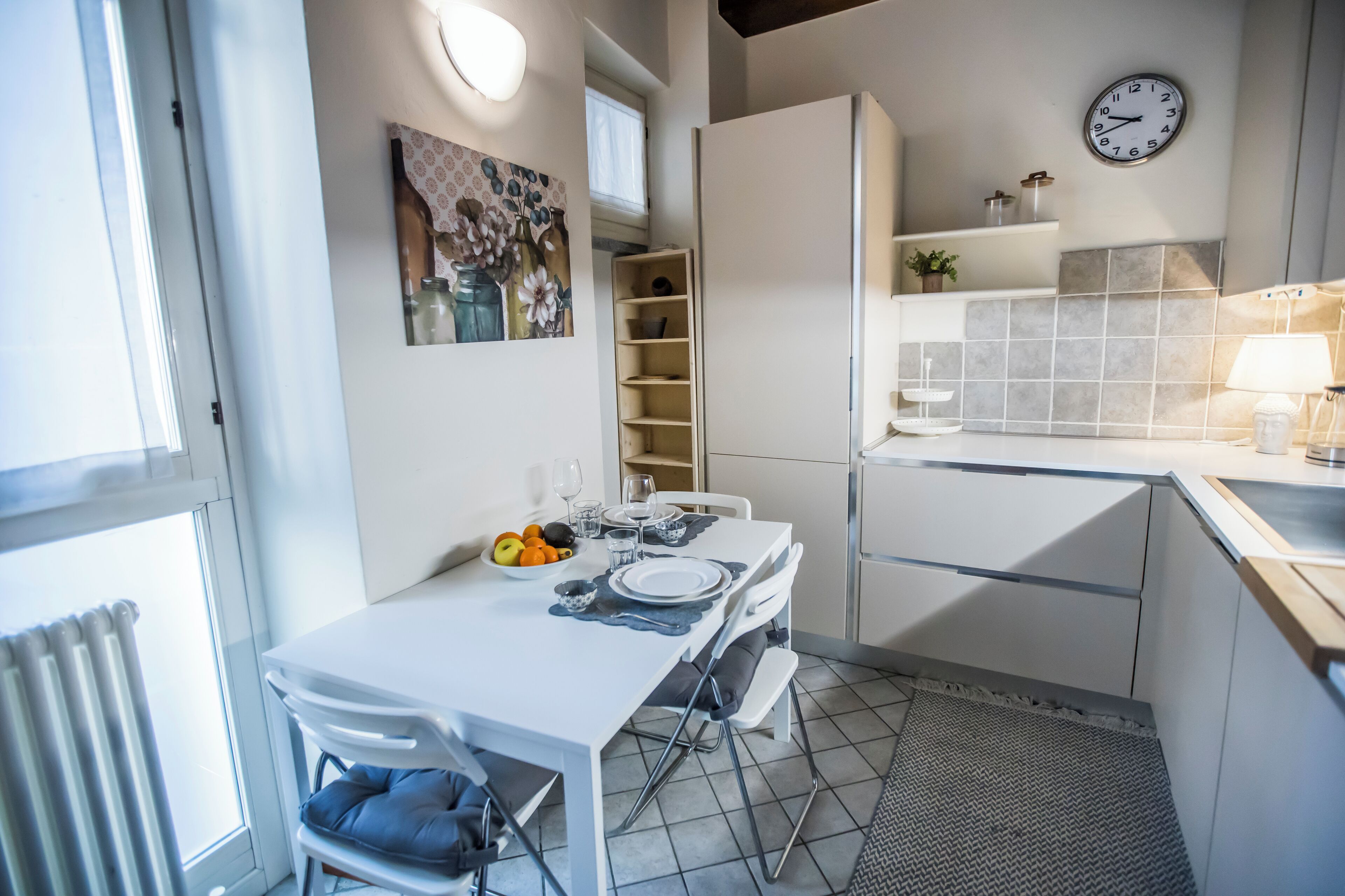 Cocina compacta con una mesa de comedor para dos personas, un reloj en la pared y un estante con adornos.