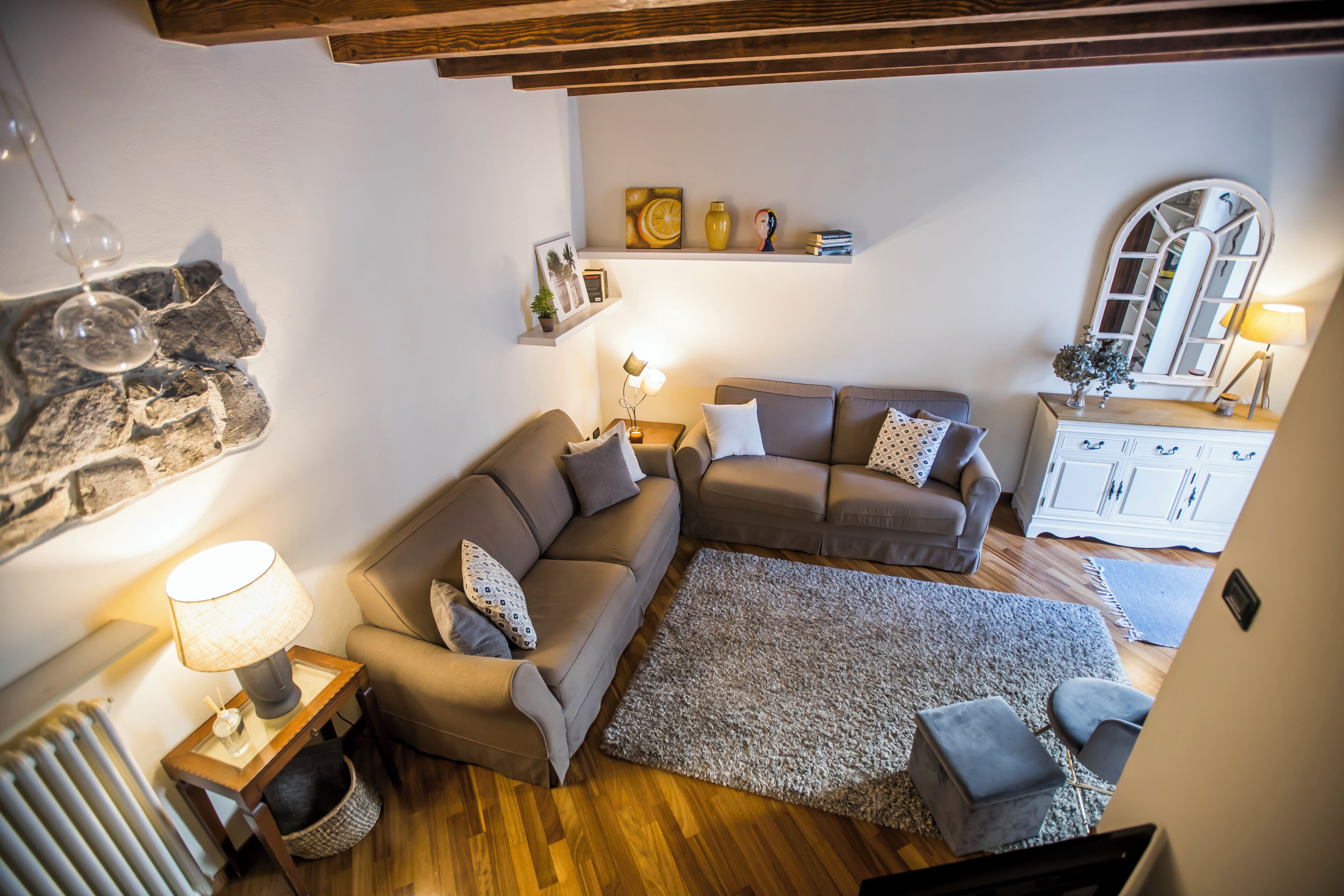A cozy living room with a sectional sofa, a small table with a lamp, a rug, and a cabinet with decorative items.