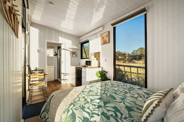 Un dormitorio con cama, escritorio, silla, ventana y vistas al exterior.