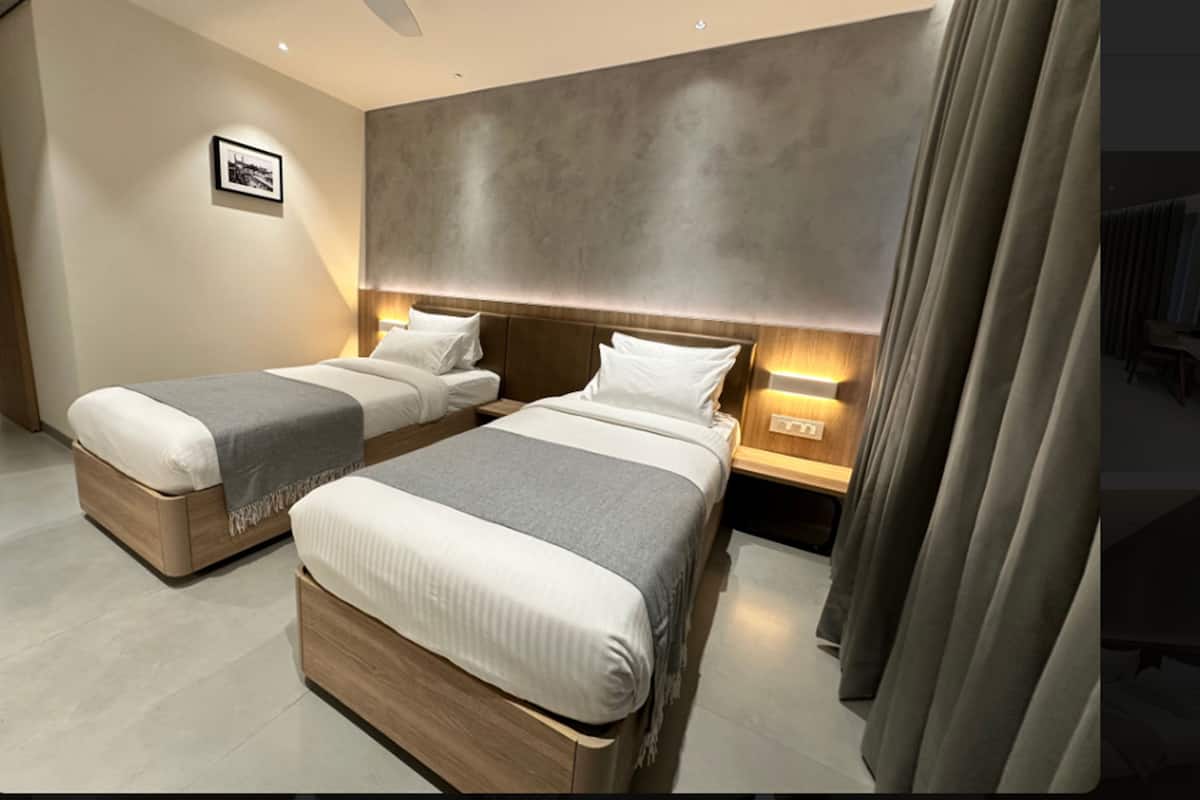 A hotel room with two beds, a large wall-mounted headboard, bedside lamps, and a framed picture on the wall.