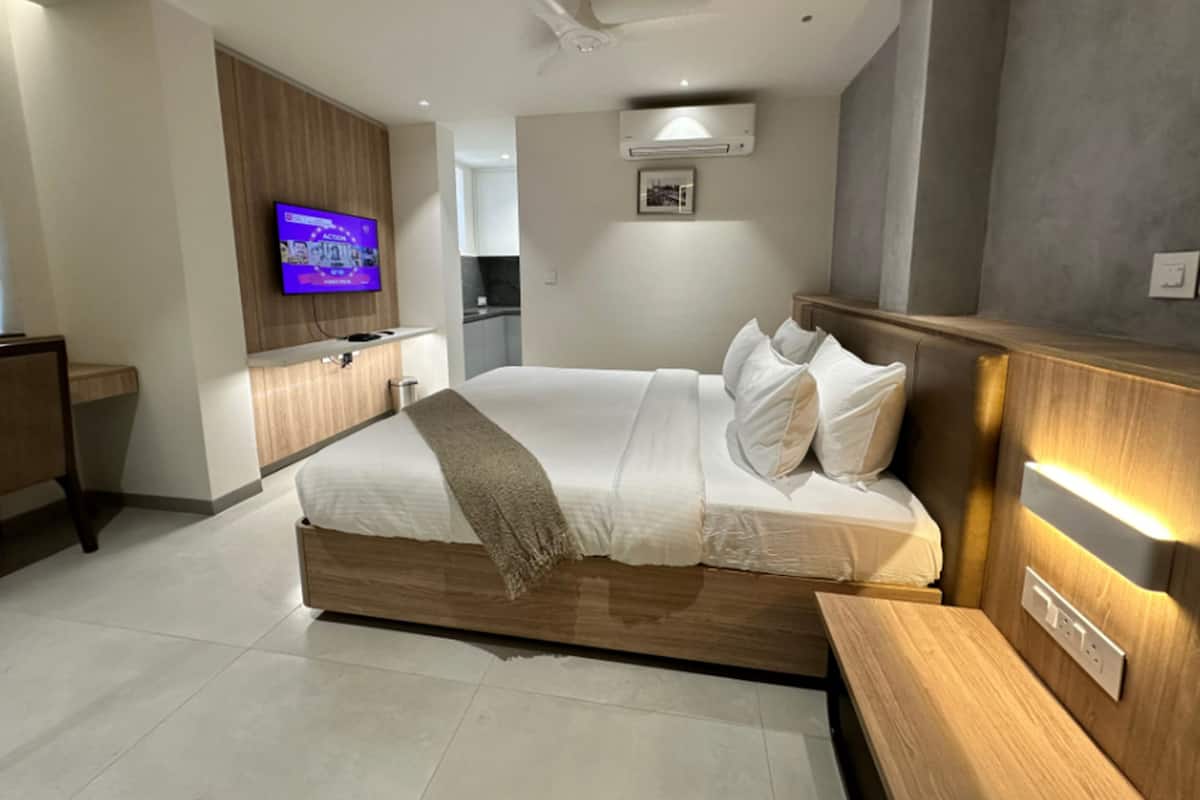 A modern hotel room with a wooden bed, a flat-screen TV, a bedside table, and a built-in heater.