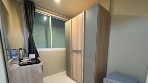 A compact hotel room with a wooden wardrobe, a small kitchenette, and a window with curtains. - Lexis Residence - Newly Renovated Rooms (Tambon Patong)
