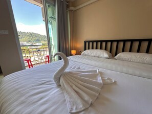 Hotelkamer met een bed, een handdoek in de vorm van een zwaan, een balkon met een rode stoel en uitzicht op een groen landschap.
