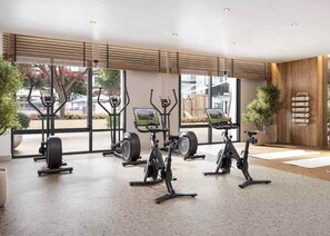 A gym with stationary bikes, a weight bench, and a large window with a view of the outside. - Bloomfields Cozy 1br Apt Town (Dubai)