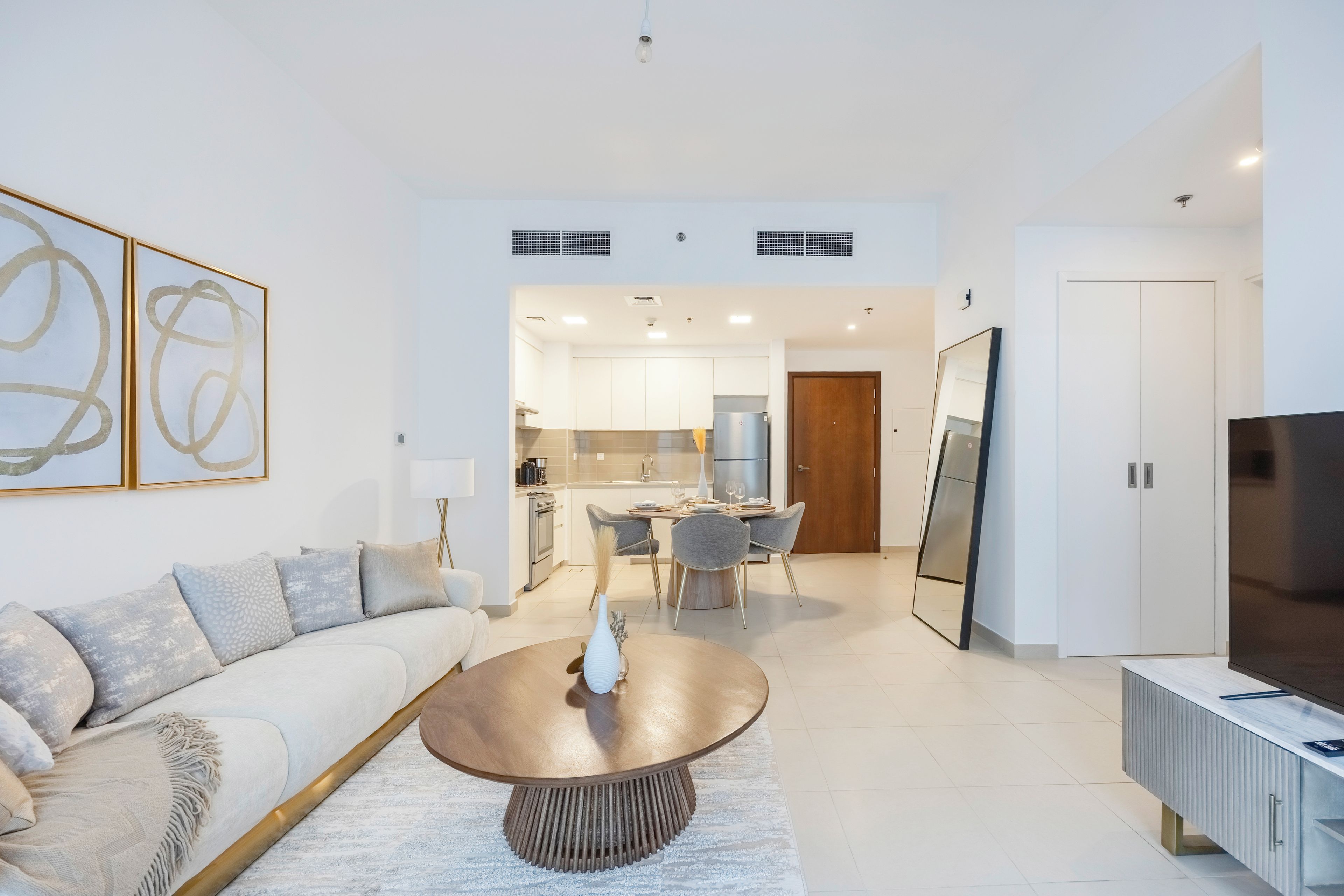 Una sala moderna con un sofá, una mesa de centro y un televisor. Se ve una cocina al fondo con un comedor.