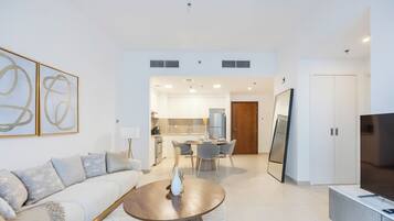 Una sala moderna con un sofá, una mesa de centro y un televisor. Se ve una cocina al fondo con un comedor.