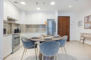 A modern kitchen with white cabinets, a built-in oven, and a dining area with a round table and four chairs. - Bloomfields Cozy 1br Apt Town (Dubai)