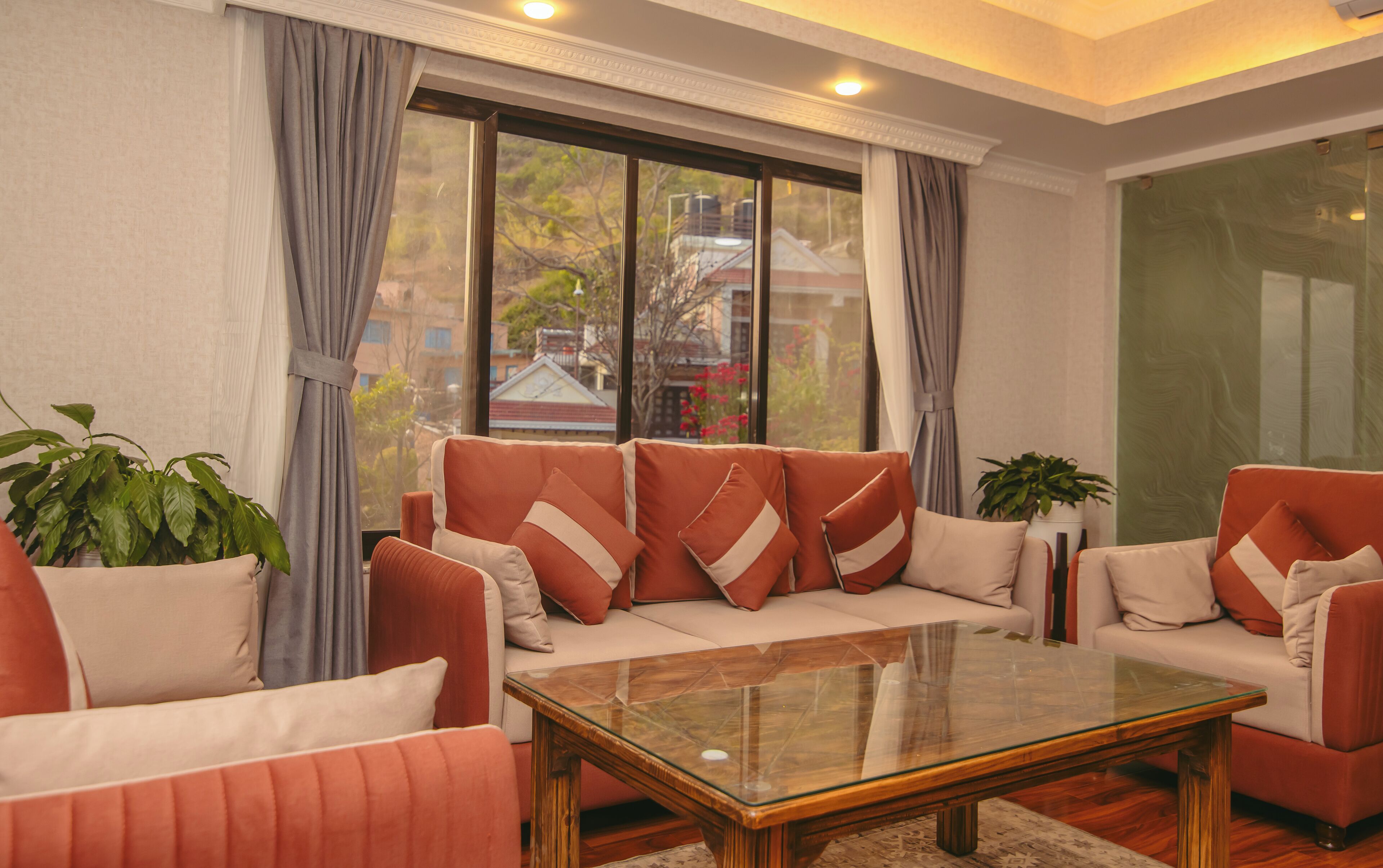 Una sala de estar moderna con un conjunto de sofás, una mesa de centro de vidrio y un ventanal con cortinas.