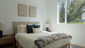 A bedroom with a bed, nightstands, a window with a view of trees, and two abstract wall art pieces. - The Marin Modern, 2BR/2BA + Private Garage (San Rafael)