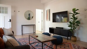 A modern living room with a sofa, a coffee table, a TV, and a potted plant. - The Marin Modern, 2BR/2BA + Private Garage (San Rafael)