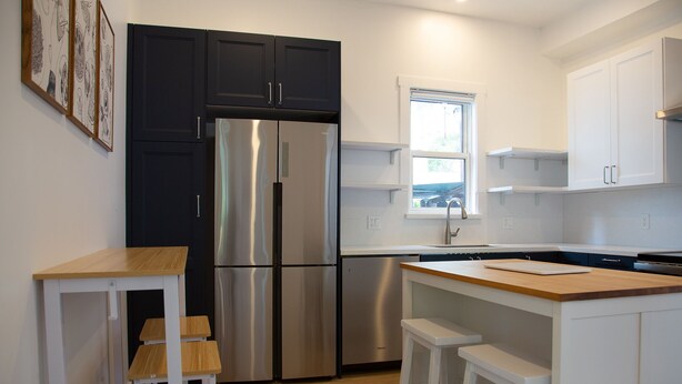 A modern kitchen with a stainless steel refrigerator, white cabinetry, and a wooden island with stools. - The Marin Modern, 2BR/2BA + Private Garage (San Rafael)