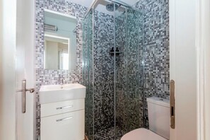 Un baño con ducha de vidrio, un lavamanos blanco y una pared con azulejos.