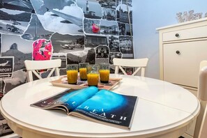 Un comedor con una mesa redonda, cuatro vasos de jugo de naranja, una revista y una pared con un collage de fotografías en blanco y negro.