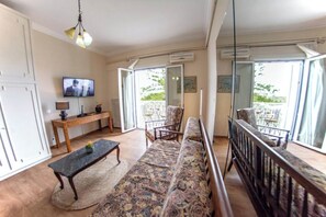 A living room with a sofa, a coffee table, a TV, and a balcony with a railing. - Corfu City View Loft - a loft with incredibly views in the historical centre (Corfu)