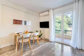 A modern dining area with a table and chairs, a flat-screen TV mounted on the wall, and a large sliding glass door leading to an outdoor balcony. - Seaview Portside apartment (Corfu)