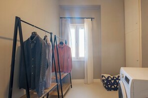 A laundry area with a washing machine, a drying rack with clothes, and a window with curtains. - Pausa Verde - Recently renovated apt, private parking (Corfu)