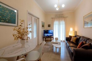 A living room with a TV, a sofa, a dining table with chairs, and a vase with dried flowers. - Casa Timos -  a stylish, comfortable retreat (Corfu)
