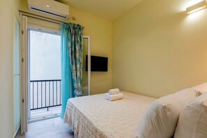 Ein Schlafzimmer mit Bett, einem an der Wand montierten Fernseher und einem Balkon mit Tür.