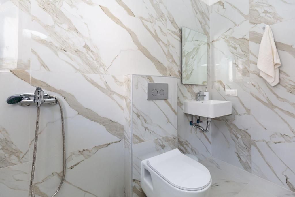 Une salle de bain avec un mur en marbre, des toilettes, un lavabo et une douche.