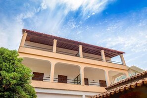 A two-story building with a balcony on the upper floor, multiple windows, and a clear sky. - Dany Apartment – First Floor with Sea View (QWQF+J59 Kassiopi, Greece)