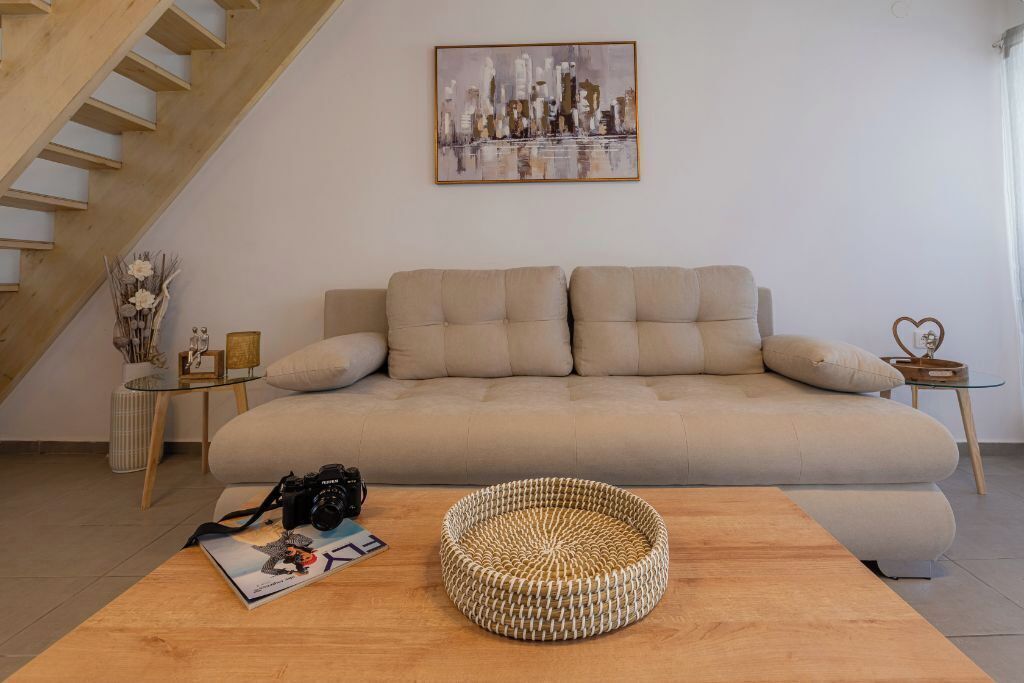 A living room with a sofa, a wooden coffee table, a camera, and a magazine.