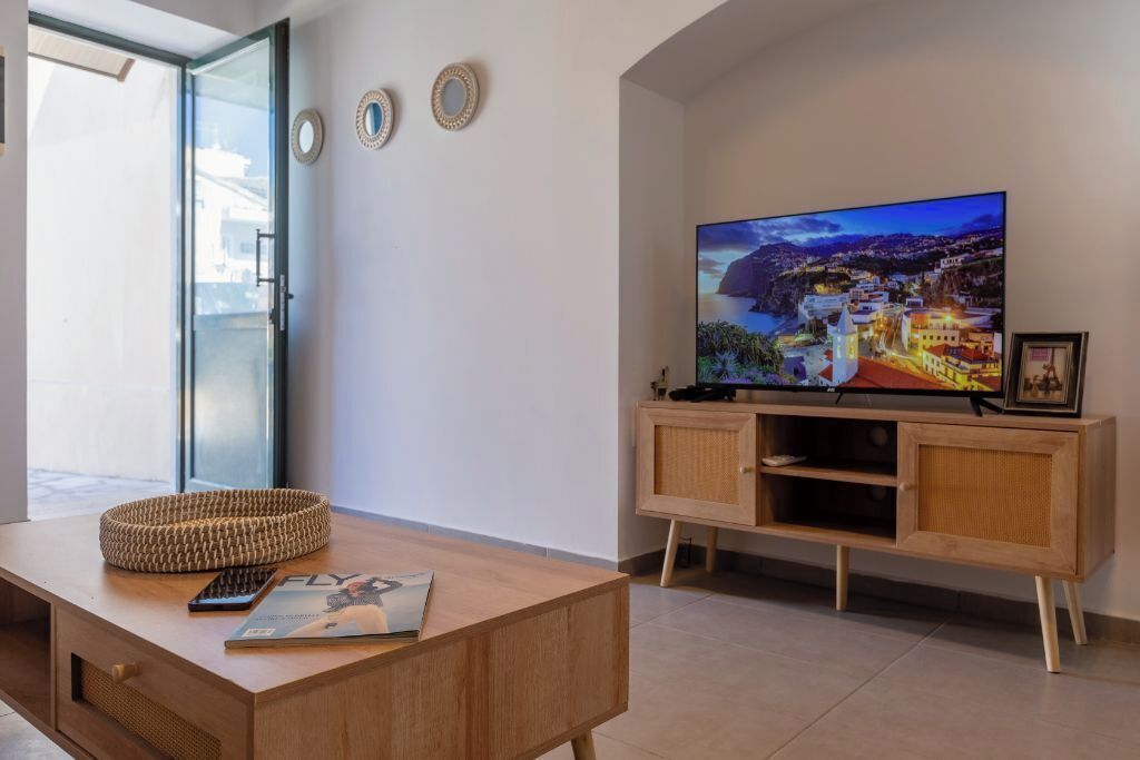 A modern living room with a wooden coffee table, a television on a wooden stand, and a view of a coastal town through the window.