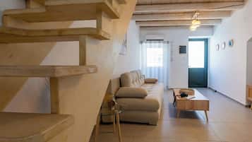 A modern living room with a wooden staircase, a beige sofa, a glass coffee table, and a wooden side table.