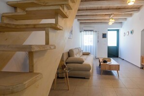 Un salon moderne avec un escalier en bois, un canapé beige, une table basse en verre et une table d’appoint en bois.
