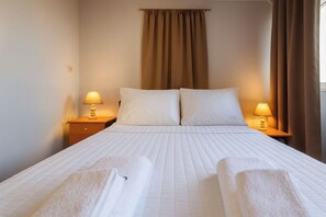 Habitació d'hotel amb un llit gran, dues làmpades de nit, una finestra amb cortines i una niseta de fusta.