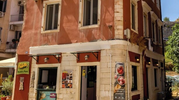 A red building with multiple windows and balconies, featuring a ground-level restaurant named "Palatte Brunch Plants". - Scala Nostra Apartment (Corfu)