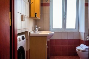 Un bany petit amb rentadora, un lavabo i un vàter.