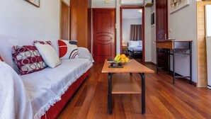 A compact living space with a sofa, a small table with fruit, and a desk with a chair. - Scala Nostra Apartment (Corfu)